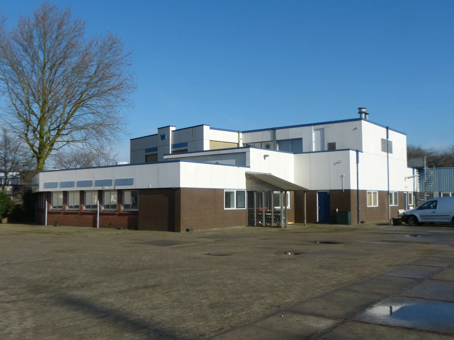 Wit-bruin bedrijfsgebouw aan de 2e Daalsedijk met parkeerterrein op de voorgrond.